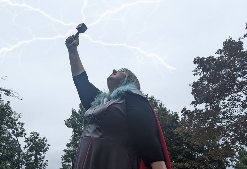 Pamela Gutman in a Thor-inspired costume holding a hammer aloft under stylized lightning